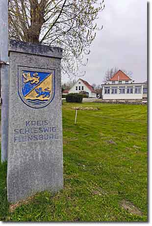 Der Grenzstein des Kreises Schleswig-Flensburg Grenzstein des Kreises Schleswig-Flensburg und das geschlossene Restaurant Fährhaus Missunde im Hintergrund an der Schlei